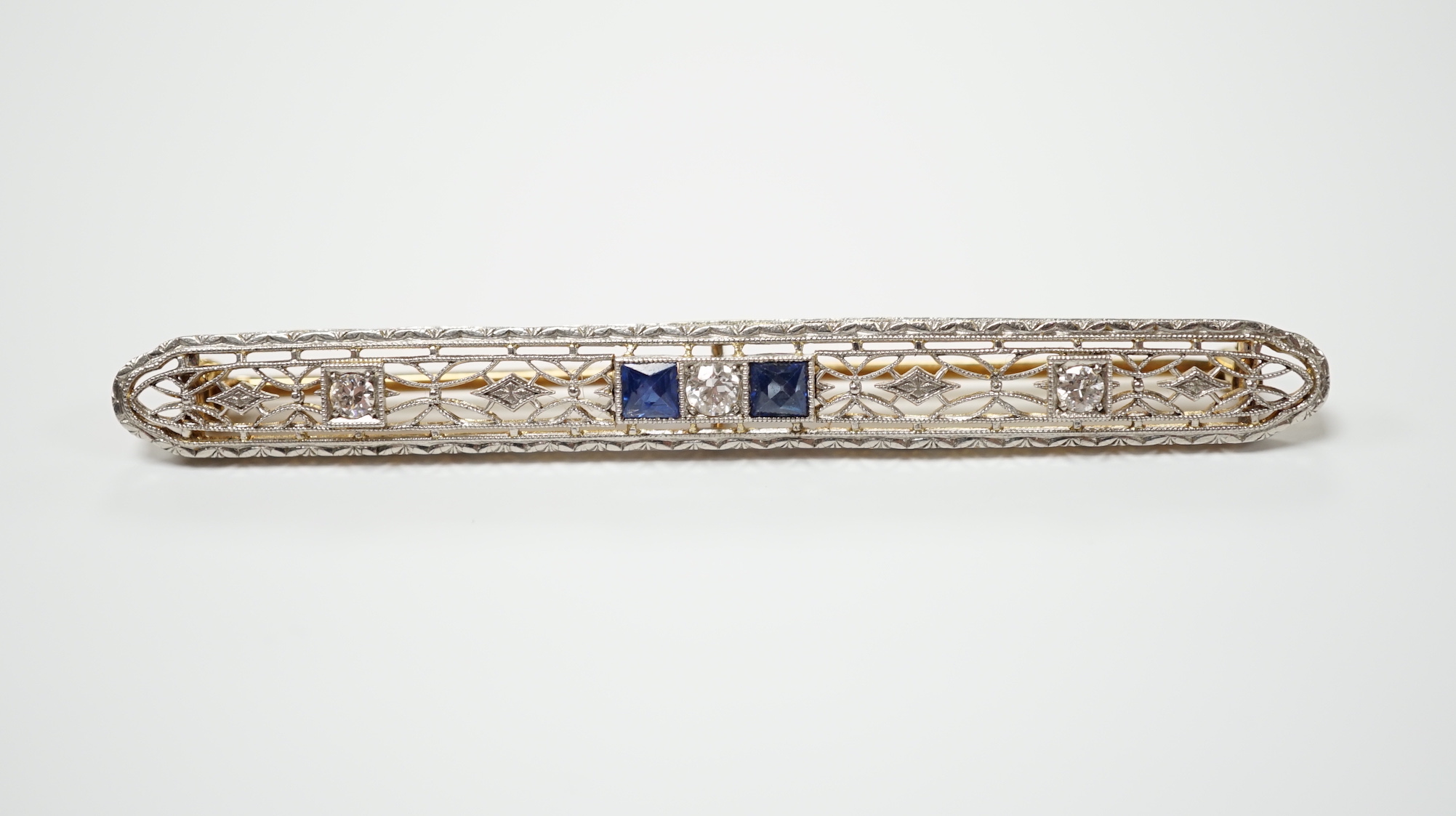 A Belle Époque style pierced 14k, sapphire and diamond cluster set bar brooch, 70mm, gross weight 5.5 grams.